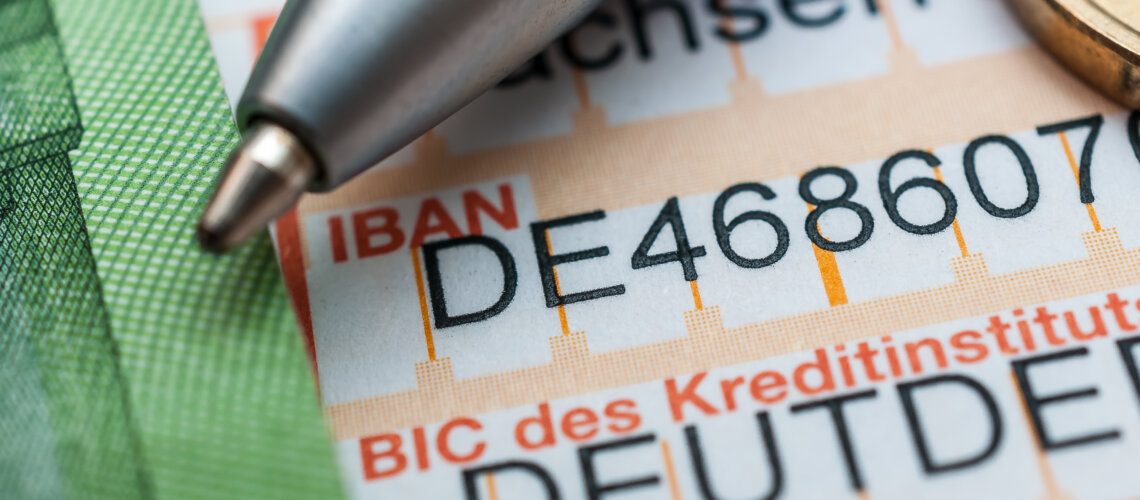 Foto eines Banküberweisungsträgers aus nächster nähe, ein Stift und ein Euro liegen auf dem papier, das teilweise mit deutschen Nummern gefüllt ist