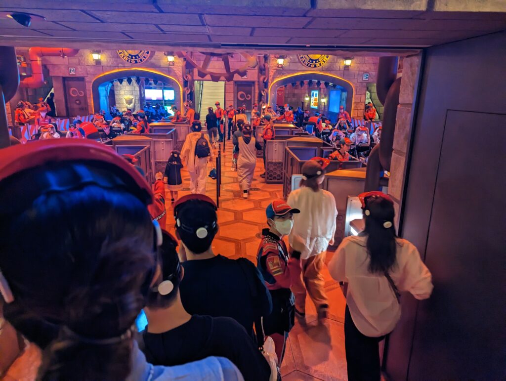 Station der Mario Kart-Attraktion in den Universal Studios Japan. Die Fahrgäste tragen eine Art Mario-Helm.