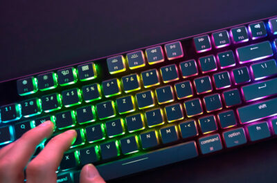 Hand auf einer Gaming-Tastatur die hell und bunt in RGB-Farben beleuchtet ist.