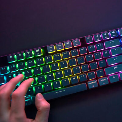Hand auf einer Gaming-Tastatur die hell und bunt in RGB-Farben beleuchtet ist.