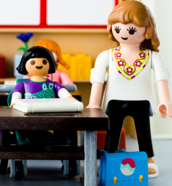 Unterrichtsszene mit einer Lehrerin, die bei einer Schülerin mit Arbeitslaptop steht mit Playmobil nachgestellt.