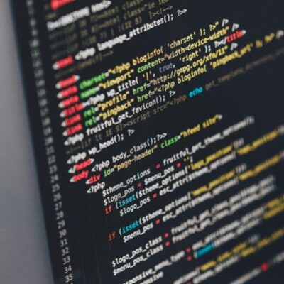 Das Bild zeigt einen Computerbildschirm mit farbigem Code, der vermutlich in einer Programmiersprache wie HTML, PHP oder JavaScript geschrieben ist. Der Code besteht aus verschiedenen Befehlen, Tags und Parametern, die in unterschiedlichen Farben angezeigt werden, um die Struktur zu verdeutlichen. Der Bildschirm wirkt dunkel, während der Code in leuchtenden Farben hervorsticht, was eine typische Arbeitsumgebung eines Programmierers oder Entwicklers darstellt.