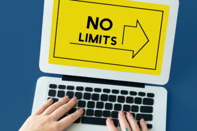 Hände auf der Tastatur eines Laptops auf dessen Bildschirm mit gelben Hintergrund eine Grafik ist deren Aufschrift "No Limits" verspricht.