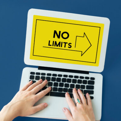 Hände auf der Tastatur eines Laptops auf dessen Bildschirm mit gelben Hintergrund eine Grafik ist deren Aufschrift "No Limits" verspricht.