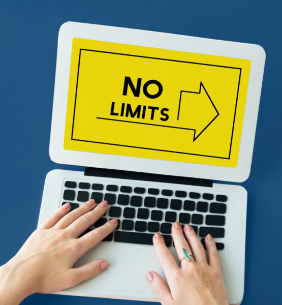 Hände auf der Tastatur eines Laptops auf dessen Bildschirm mit gelben Hintergrund eine Grafik ist deren Aufschrift "No Limits" verspricht.